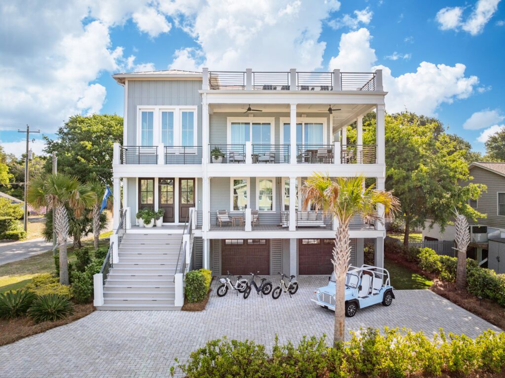 Luxury coastal vacation home with modern architecture, three balconies, palm trees, and a driveway featuring a Moke vehicle and electric bikes in Isle of Palms, South Carolina.